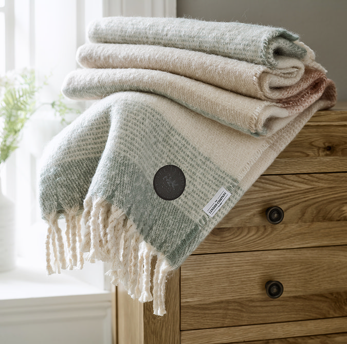 blush pink and pale green throw folded on top of light brown wood chest of drawers