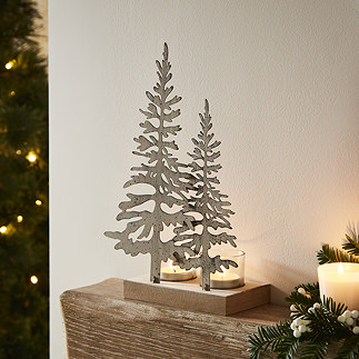 two metal rustic silhouette trees on wooden stand with glass tealights, stood on a mantlepiece.