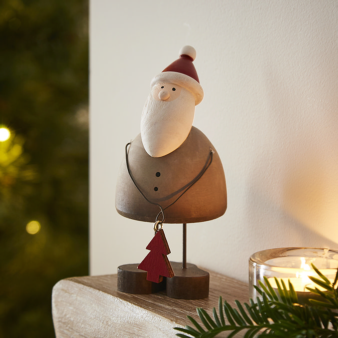 rustic wooden small santa decoration, holding a small wooden star and stood on the edge of a light oak mantlepiece.