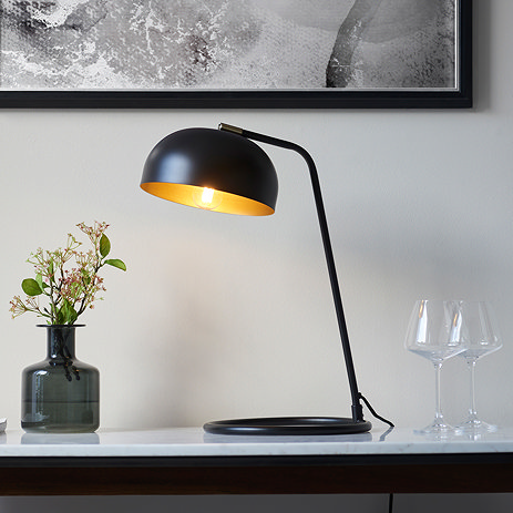 image of black table lamp with domed shade emitting warm light on a modern sideboard in front of a grey wall