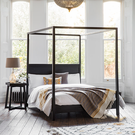 image of four poster black wooden bed with rug under it
