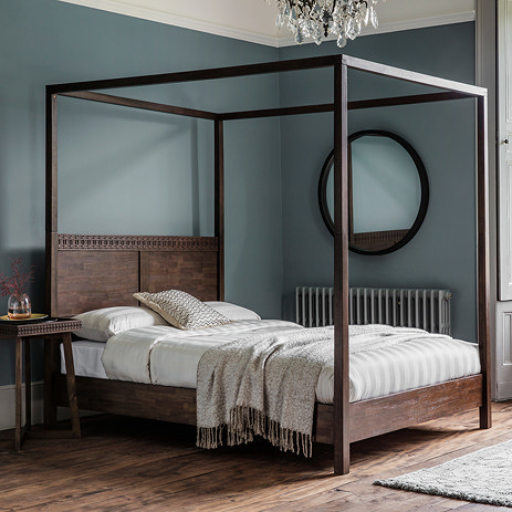 image of four poster brown wooden bed against duck egg blue wall