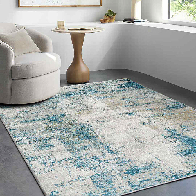 image of abstract teal and ivory rug in a small front room with modern armchair on top of it in the left corner, in front of a window