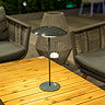 image of tall thin dark grey table lamp on wooden garden table at night, shining warm light