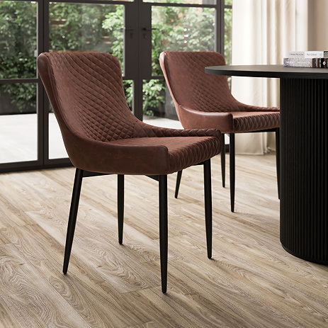 image of two faux leather dining chairs with black legs tucked under round black dining table