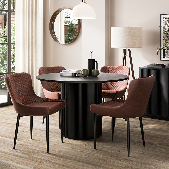 image of four faux leather dining chairs with black legs tucked under black round dining table