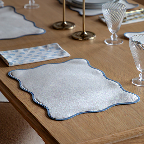 image of cream placemat with a blue scalloped edge, on an oak table