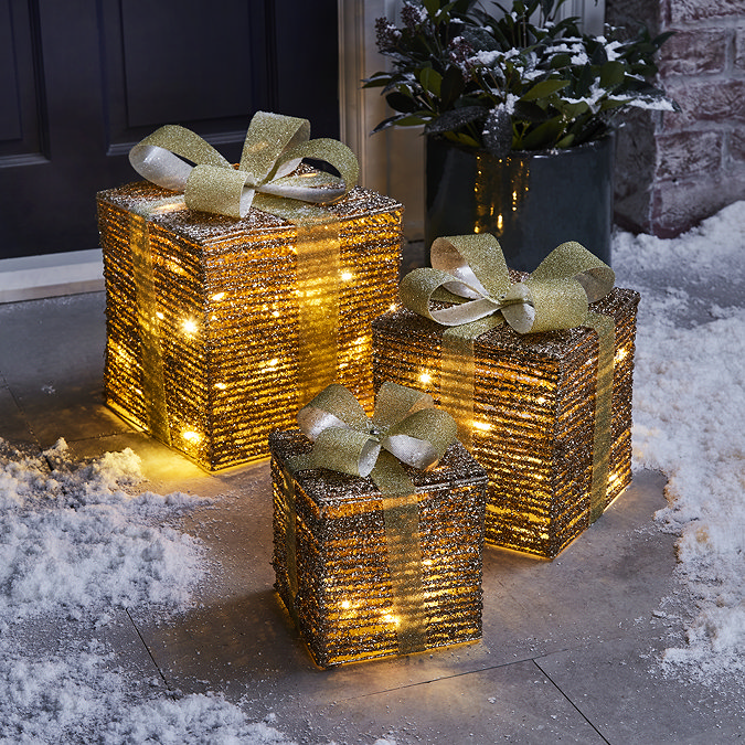 set of three gold parcels lit up with warm white LEDs, outside a front door on a snowy driveway.