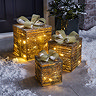 set of three gold parcels lit up with warm white LEDs, outside a front door on a snowy driveway.