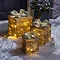 set of three gold parcels lit up with warm white LEDs, outside a front door on a snowy driveway.