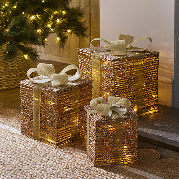 set of three gold parcels lit up with warm white LEDs, outside a front door on a snowy driveway.