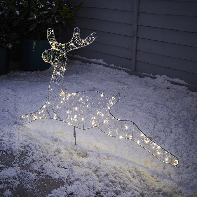 image of single reindeer stake light lit up outside a house in the snow at night