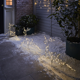 set of 3 reindeer shape with warm white LEDs stakes in ground outside a house at night
