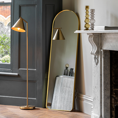 image of full length gold floor mirror leaning against a cream wall with gold floor lamp standing next to it