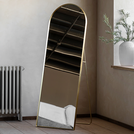 image of arched gold mirror with supportive stand on the back, in the corner of a room