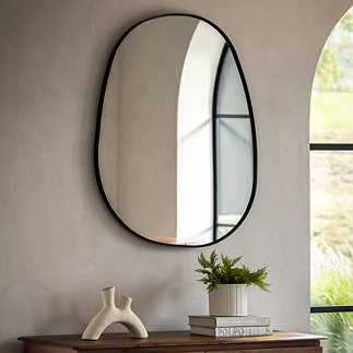 image of pebble shaped black frame mirror on sandstone wall behind sofa