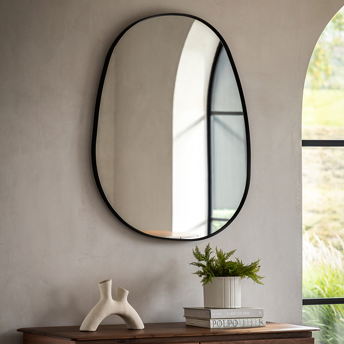 image of pebble shaped black frame mirror on sandstone wall behind sofa