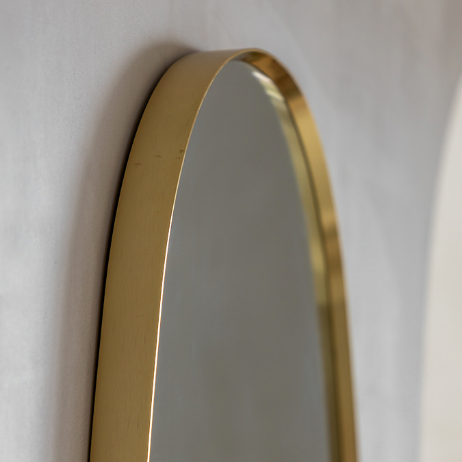 close up on smooth arched top of pebble shaped wall mirror with gold edge