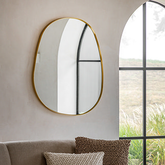image of gold pebble shaped mirror on sandstone wall behind a sofa