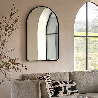 image of black frame mirror with smooth curved top on a sandstone wall behind a mirror