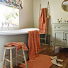 wide shot of bathroom with amber towels draped over the bath, on a stool, hung up on a wall, with coordinating bath mat on the floor