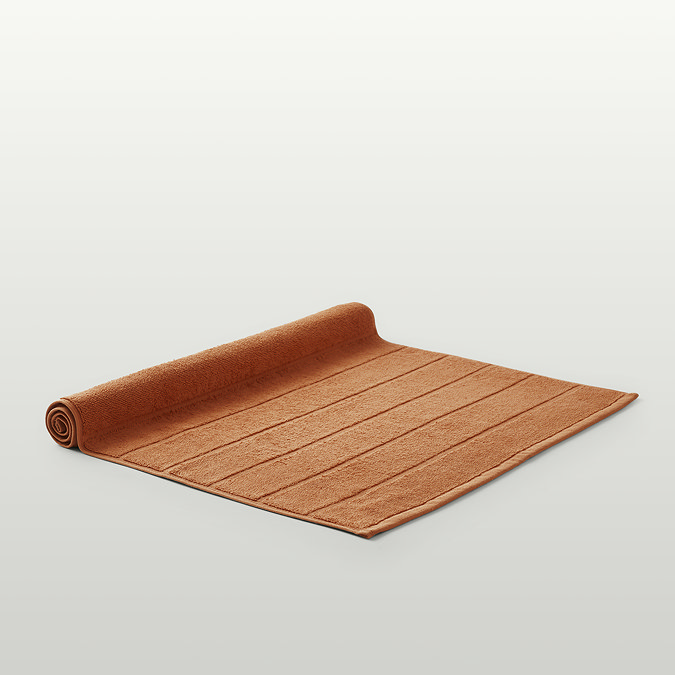 image of amber bath mat slightly rolled up at the end, on light grey background