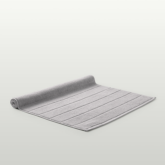 image of light grey bath mat slightly rolled up at end, on light grey background