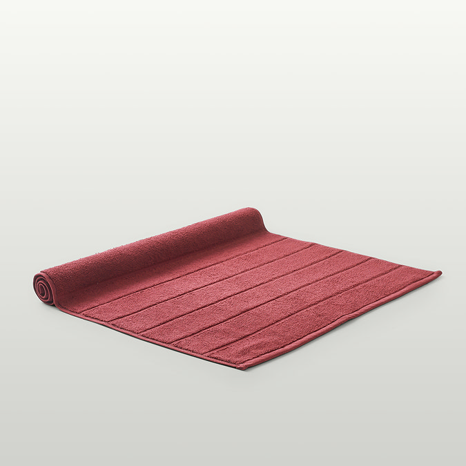 image of light red bath mat slightly rolled up at the end, on light grey background