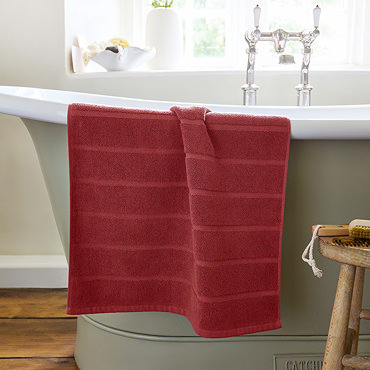 image of light red bath mat slightly rolled up at the end, on light grey background
