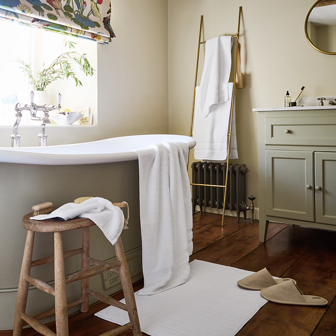 wide shot of bathroom full of white cotton towels, with matching bath mat on floor
