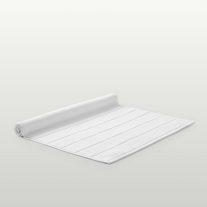 image of white bath mat rolled up on one end, on light grey background