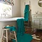 wide shot of bathroom with vivid teal towels draped over the bath, on a stool, hung up on a wall, with coordinating bath mat on the floor