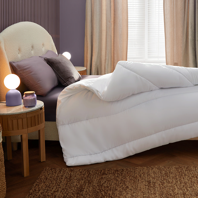 side on image of thick uncovered duvet folded back at the corner on top of purple sheet and pillows