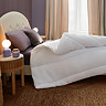 side on image of thick uncovered duvet folded back at the corner on top of purple sheet and pillows
