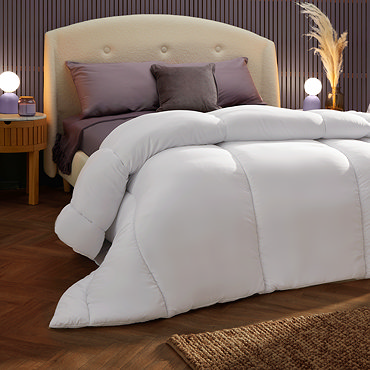side on image of thick uncovered duvet folded back at the corner on top of purple sheet and pillows