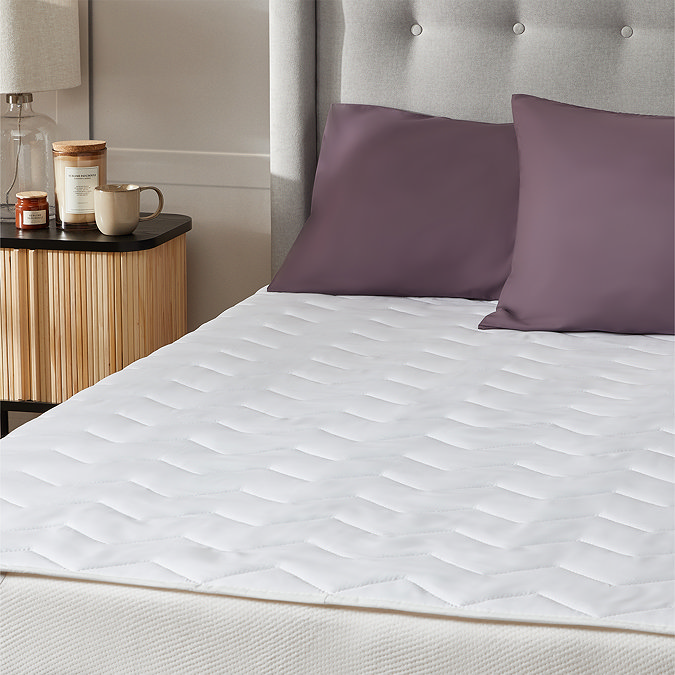 close up on one half of a bed showing mattress protector with two purple pillows at the top of the bed