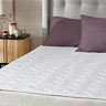 close up on one half of a bed showing mattress protector with two purple pillows at the top of the bed
