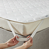 close up of a person's two hands stretching the elastic band of a mattress topper over a corner of the bed to secure it