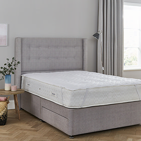 wide image of mattress protector atop a mattress on a bed with purple headboard