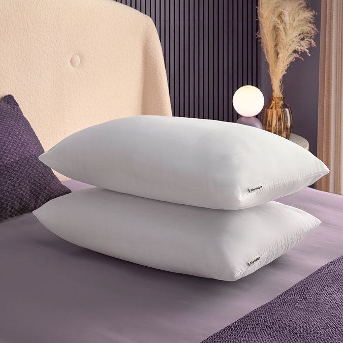 two plush white pillows stacked on top of each other on top of a purple bed sheet