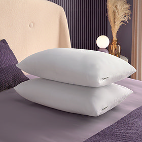two plush white pillows stacked on top of each other on top of a purple bed sheet