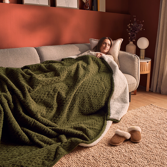 image of woman reclining on sofa, covered in large green cable knit blanket
