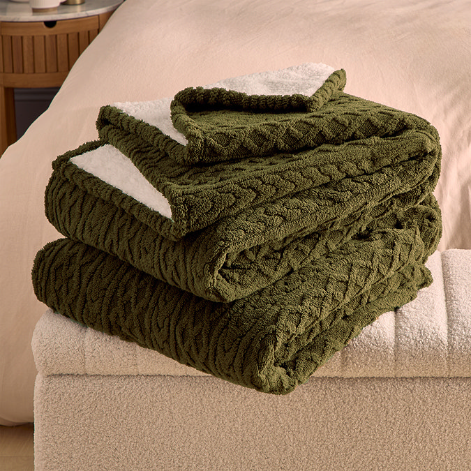 green cable knit blanket folded up and resting on the arm of a cream sofa