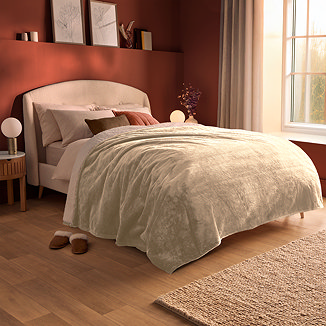 large natural coloured blanket draped over a bed's duvet cover