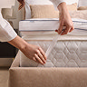 person stretching band of mattress topper around the edge of the mattress