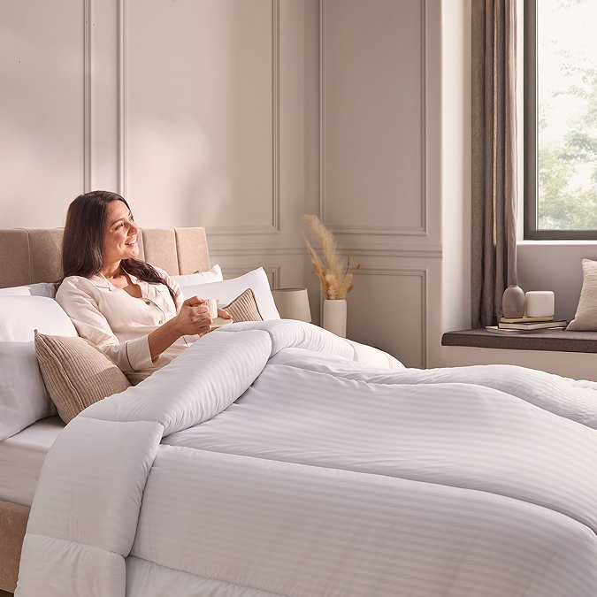 woman sat under thick duvet with a mug of coffee