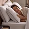 side on image of woman resting in bed with head on pair of hotel pillows, white with blue edging