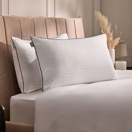 pair of hotel pillows, white with blue piping, resting at the top of a bed