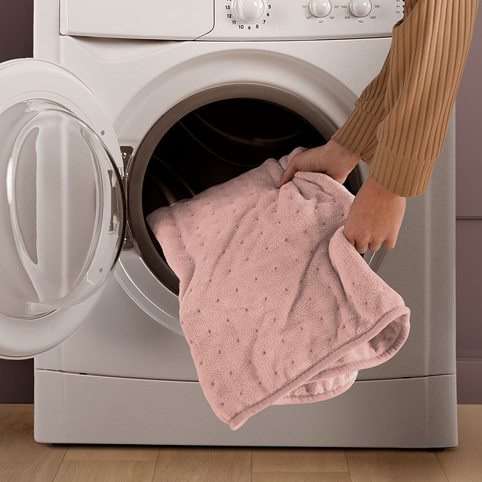 image of blush pink heated throw being placed into a washing machine