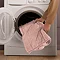 image of blush pink heated throw being placed into a washing machine
